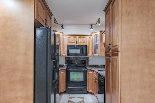 kitchen with dark stone countertops, black appliances, light tile patterned floors, and track lighting