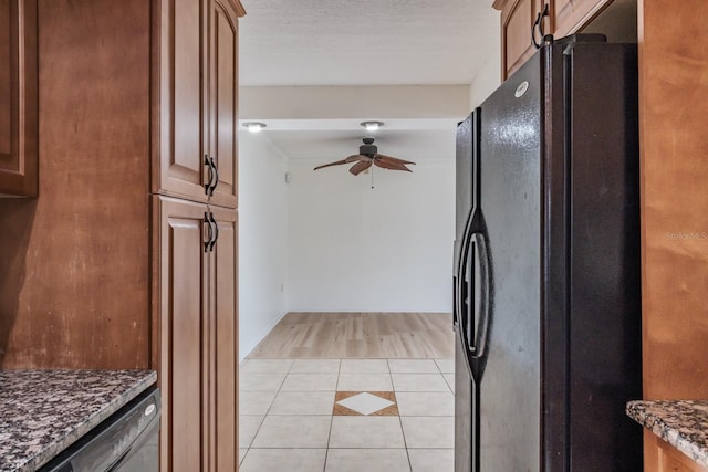 kitchen with a textured ceiling, light tile patterned floors, ceiling fan, black fridge, and dark stone counters