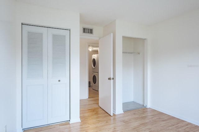 unfurnished bedroom with a closet, stacked washer and dryer, and light hardwood / wood-style floors