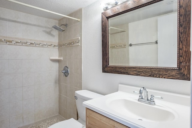 bathroom with tiled shower, vanity, toilet, and a textured ceiling