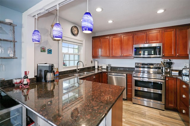 kitchen with light wood finished floors, stainless steel appliances, a sink, dark stone countertops, and a peninsula