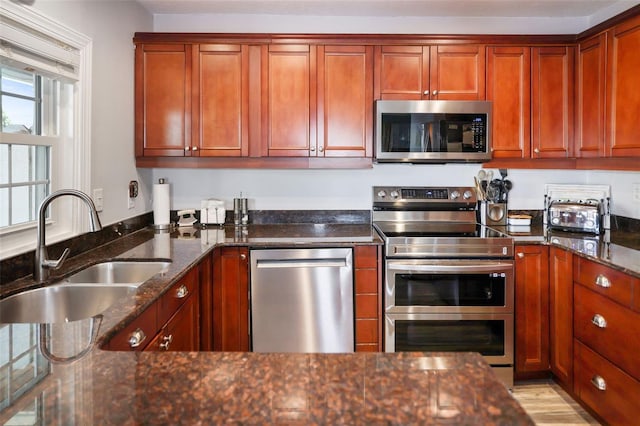 kitchen with appliances with stainless steel finishes, dark stone counters, brown cabinets, and a sink