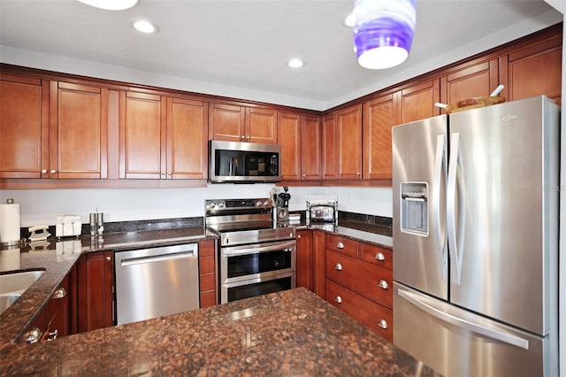 kitchen featuring brown cabinetry, appliances with stainless steel finishes, dark stone counters, and recessed lighting