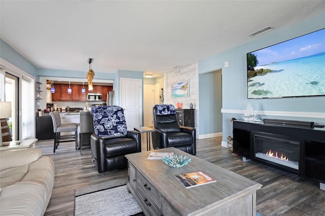 living area with dark wood-style floors, baseboards, visible vents, and a glass covered fireplace