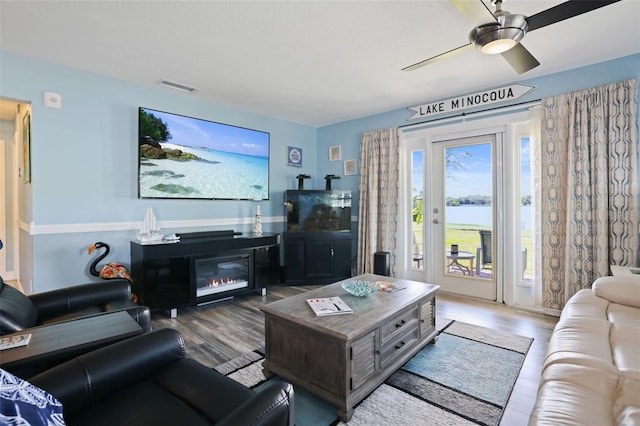 living room featuring ceiling fan, a glass covered fireplace, wood finished floors, and visible vents