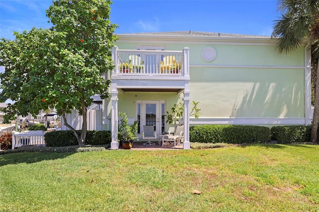 view of front facade with a front yard, fence, a balcony, and stucco siding