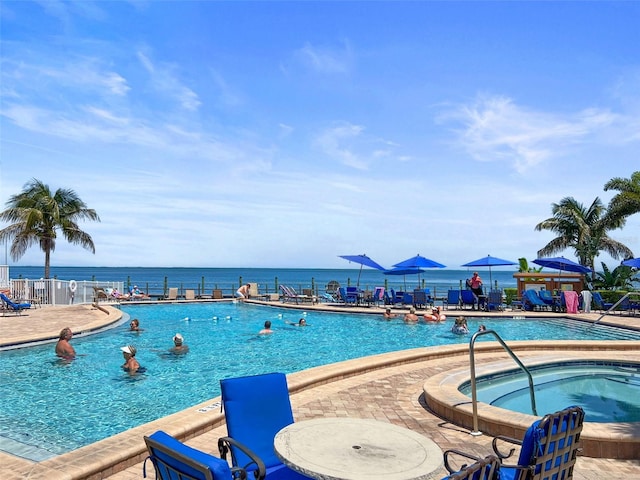 community pool with a patio, a community hot tub, fence, and a water view