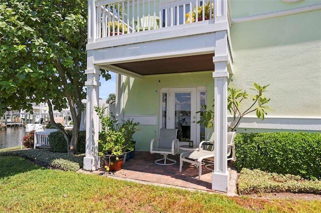 doorway to property with a balcony, a water view, stucco siding, and french doors