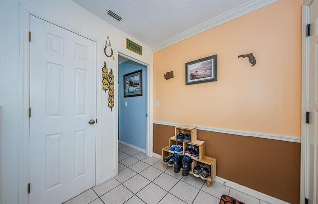 hall with a textured ceiling, light tile patterned flooring, and ornamental molding