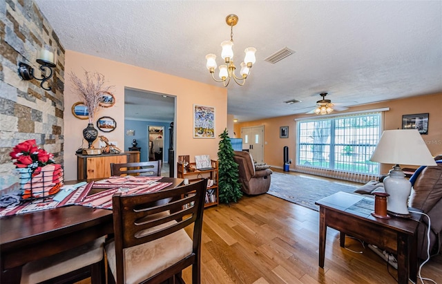 dining room with ceiling fan with notable chandelier, a textured ceiling, and hardwood / wood-style floors