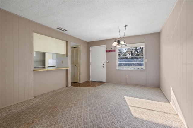 unfurnished dining area featuring a textured ceiling, light carpet, wooden walls, and a chandelier