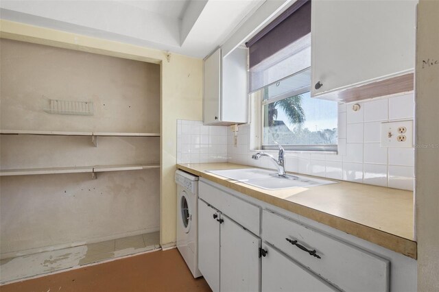 kitchen with washer / clothes dryer, backsplash, white cabinetry, and sink