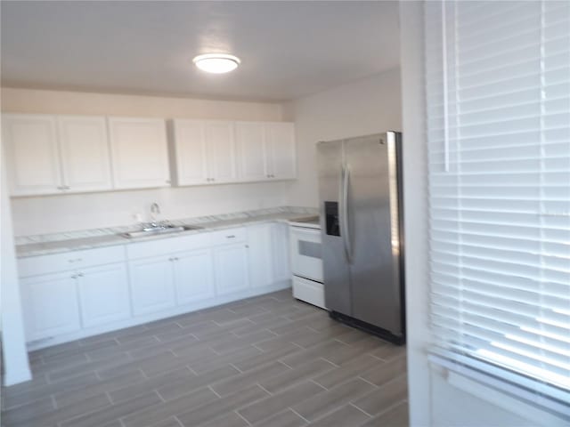 kitchen featuring white cabinets, stainless steel fridge, sink, and white stove