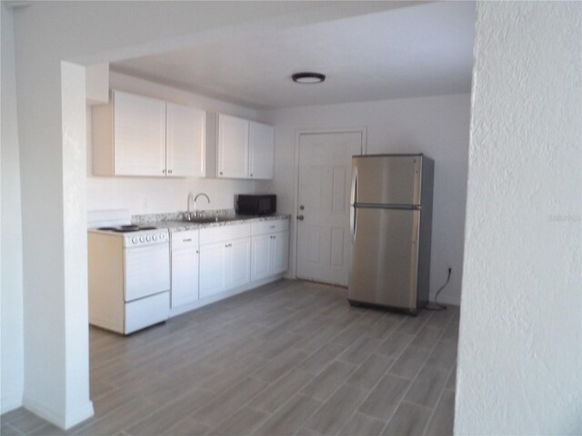 kitchen featuring hardwood / wood-style floors, stainless steel fridge, white range oven, sink, and white cabinets