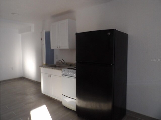 kitchen with white stove, sink, white cabinets, and black fridge