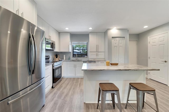 kitchen with light wood-type flooring, white cabinetry, stainless steel appliances, and light stone countertops