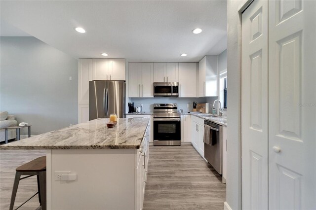 kitchen with stainless steel appliances, light stone counters, sink, a kitchen island, and white cabinets