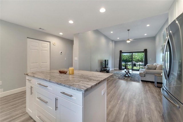 kitchen with stainless steel refrigerator, ceiling fan, light stone counters, light wood-type flooring, and white cabinets