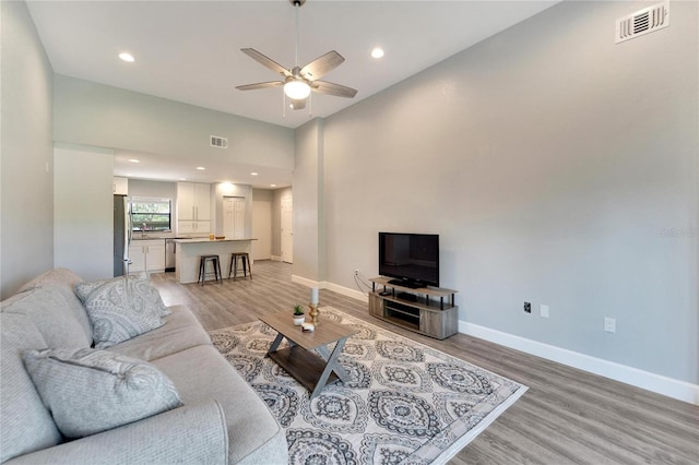 living room with a high ceiling, ceiling fan, and light hardwood / wood-style floors