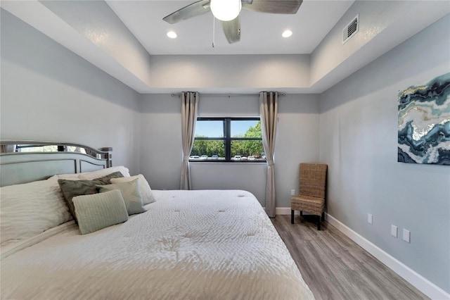 bedroom with ceiling fan, wood-type flooring, and a tray ceiling