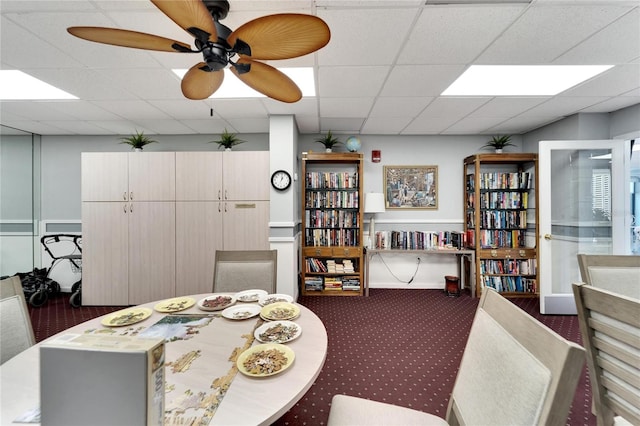 carpeted dining space featuring ceiling fan and a drop ceiling