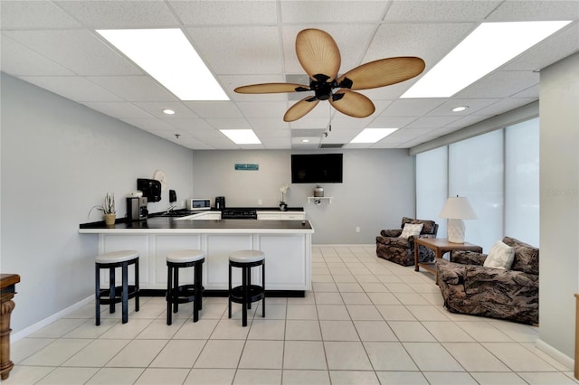 kitchen featuring a drop ceiling, a kitchen bar, light tile patterned floors, kitchen peninsula, and ceiling fan