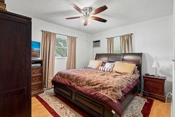 bedroom with a wall mounted AC, ceiling fan, and light hardwood / wood-style floors