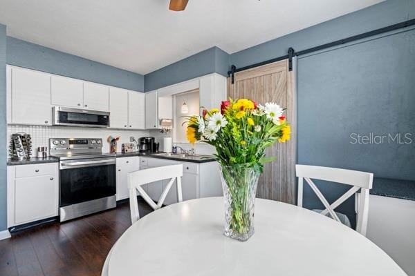 kitchen with a barn door, appliances with stainless steel finishes, dark hardwood / wood-style floors, and white cabinetry