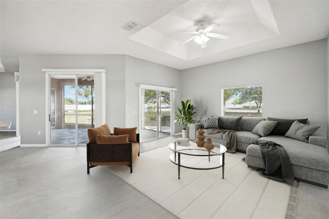 living room with ceiling fan, a raised ceiling, and a textured ceiling