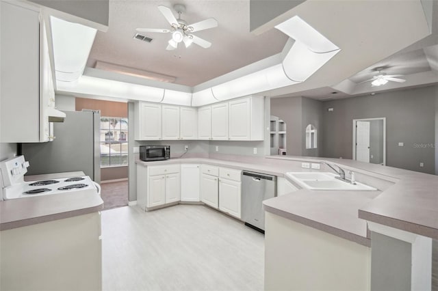 kitchen featuring kitchen peninsula, a raised ceiling, white cabinets, appliances with stainless steel finishes, and sink