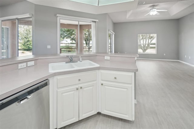 kitchen with sink, white cabinetry, ceiling fan, stainless steel dishwasher, and a tray ceiling