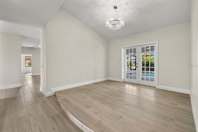 unfurnished room with light hardwood / wood-style flooring, vaulted ceiling, an inviting chandelier, and french doors