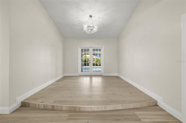 spare room featuring french doors, light hardwood / wood-style flooring, and an inviting chandelier