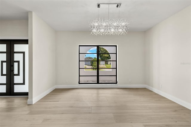 empty room with an inviting chandelier, light wood-type flooring, and french doors