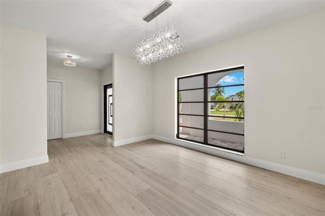 unfurnished room featuring an inviting chandelier and light hardwood / wood-style floors