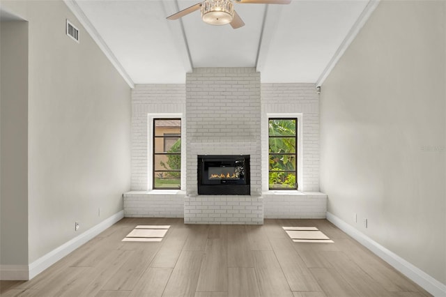 unfurnished living room featuring a fireplace, light hardwood / wood-style flooring, brick wall, ceiling fan, and beam ceiling