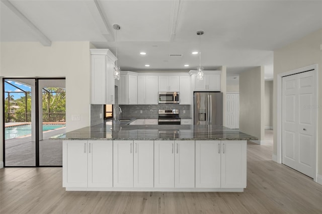 kitchen with light wood-type flooring, dark stone counters, stainless steel appliances, sink, and decorative backsplash