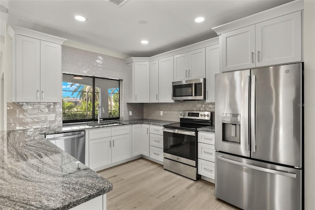 kitchen featuring light wood-type flooring, tasteful backsplash, white cabinetry, sink, and appliances with stainless steel finishes