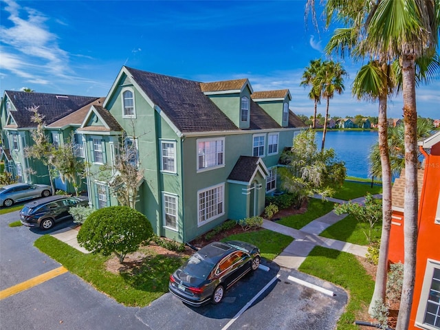 view of front of property with a water view, roof with shingles, a residential view, stucco siding, and uncovered parking