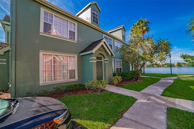 view of front facade featuring a water view, a front yard, and stucco siding