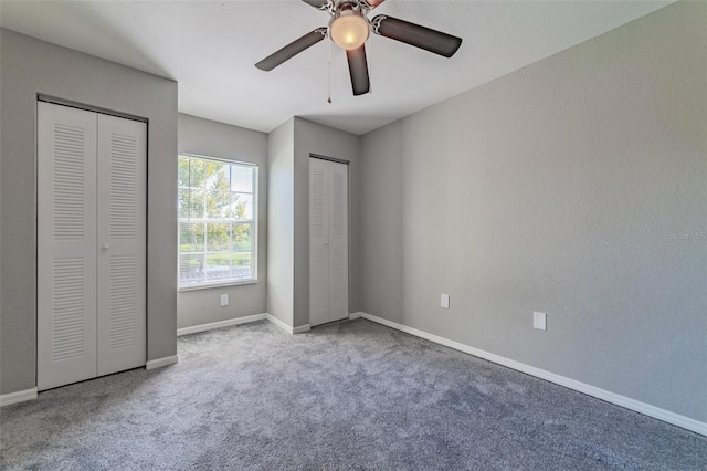 unfurnished bedroom featuring carpet flooring, two closets, a ceiling fan, and baseboards