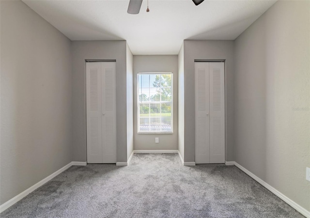 unfurnished bedroom featuring carpet, ceiling fan, baseboards, and two closets