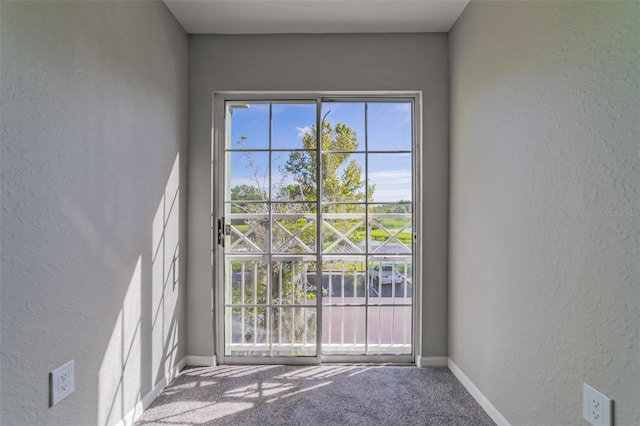 doorway to outside featuring a textured wall, baseboards, a wealth of natural light, and carpet flooring