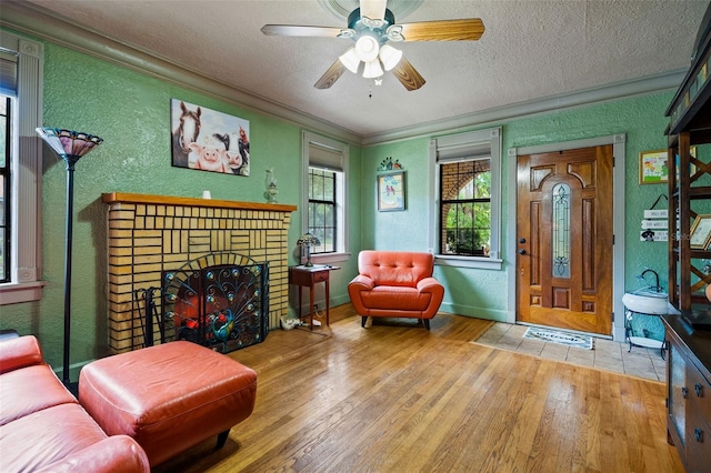 living room featuring a brick fireplace, ceiling fan, light hardwood / wood-style floors, and a textured ceiling