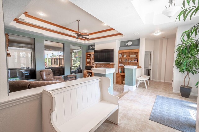 living room featuring a tray ceiling, light tile patterned floors, ornamental molding, and ceiling fan