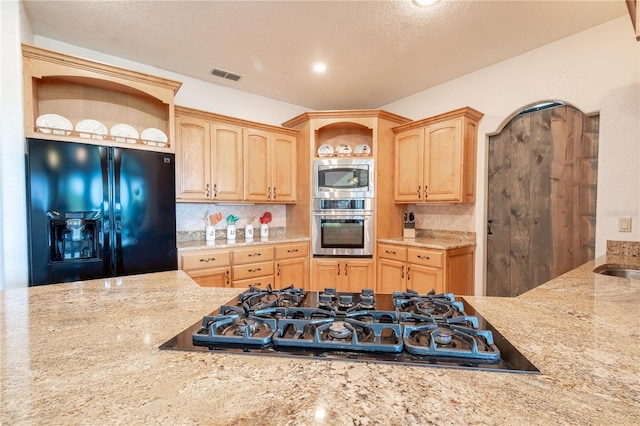 kitchen featuring a textured ceiling, light stone countertops, backsplash, appliances with stainless steel finishes, and light brown cabinets