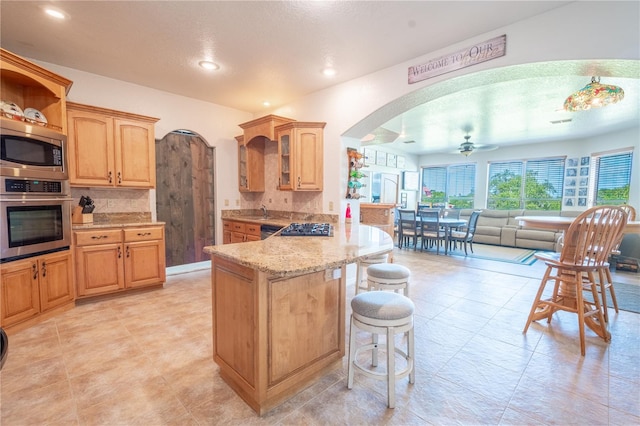 kitchen featuring a kitchen bar, stainless steel appliances, kitchen peninsula, ceiling fan, and light stone counters