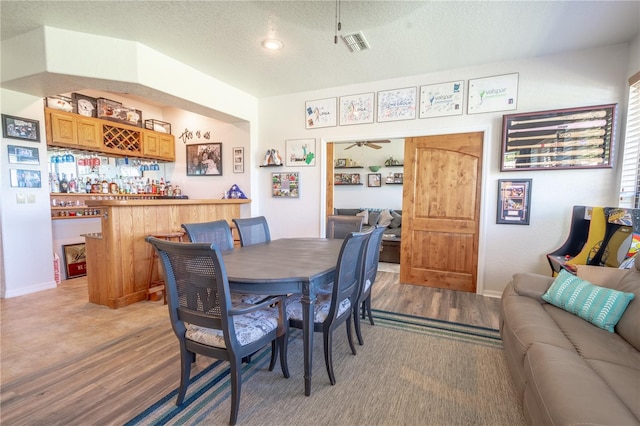 dining space with a textured ceiling, ceiling fan, bar area, and light wood-type flooring