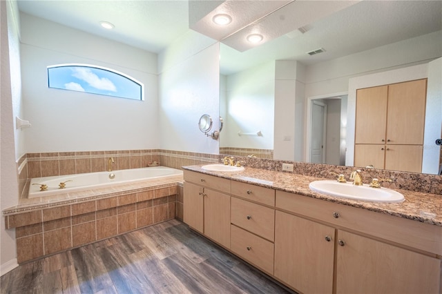 bathroom with tiled tub, vanity, and wood-type flooring