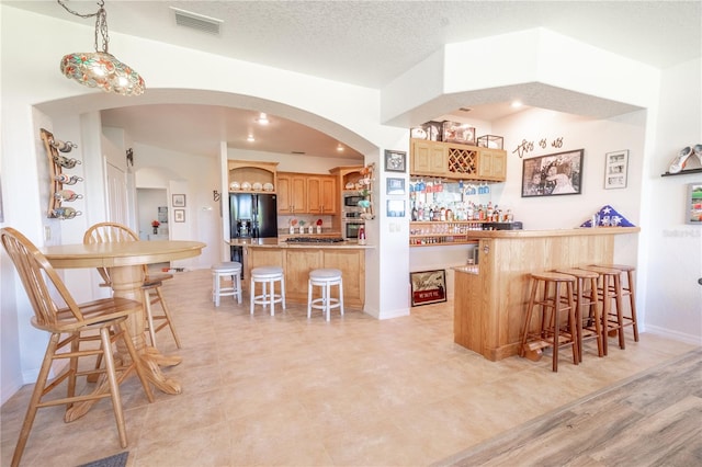 kitchen with a textured ceiling, light hardwood / wood-style flooring, appliances with stainless steel finishes, a kitchen bar, and kitchen peninsula